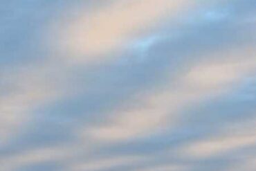 Morgenhimmel, blau-weiß quergestreift von den Wolken, im Hintergrund unten rechts klein der Mont St. Michel